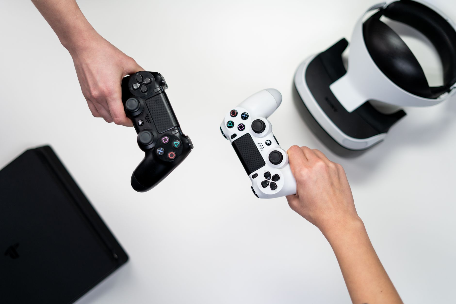 Deux mains tenant des manettes de jeu vidéo au-dessus d’une table blanche.
