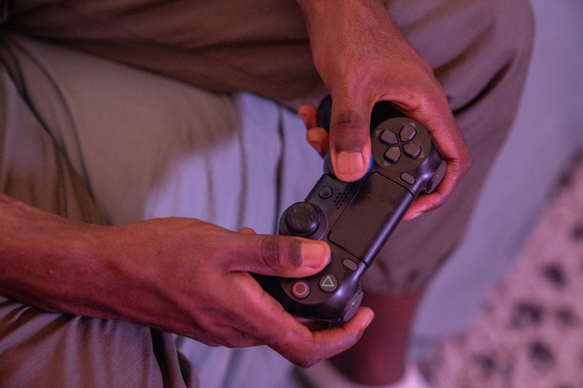 Gros plan sur deux mains tenant une manette, un contrôleur de jeu vidéo noir, dans une lumière rosée