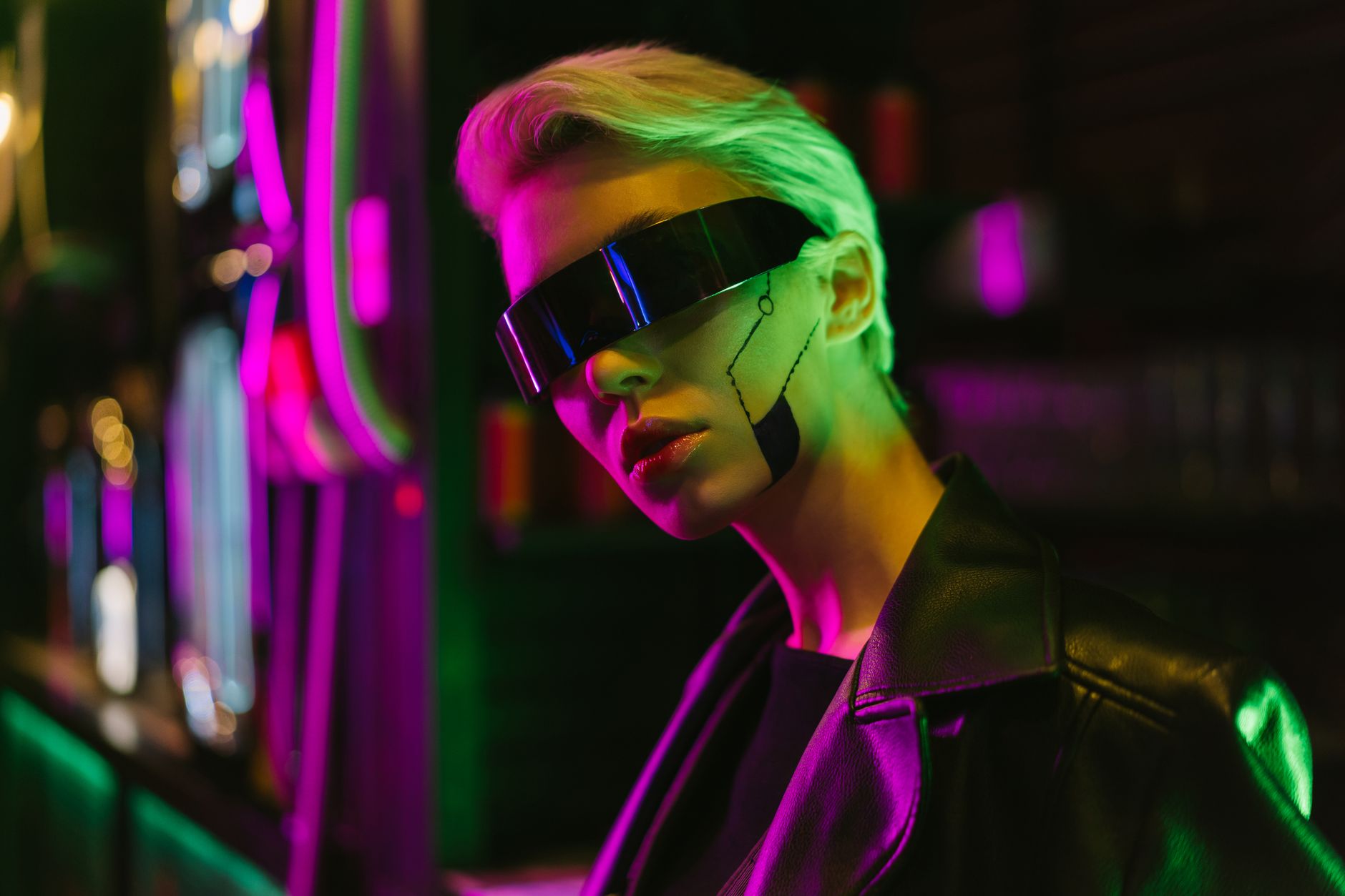 Personne aux cheveux courts portant une visière futuriste noire et une veste en cuir, éclairée par des néons roses et verts.