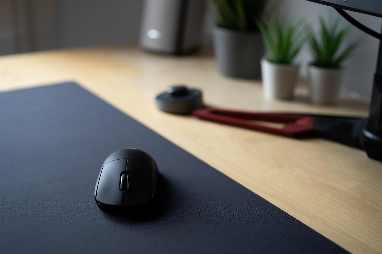 Une souris de jeu noire posée sur un tapis de souris, sur un bureau en bois clair